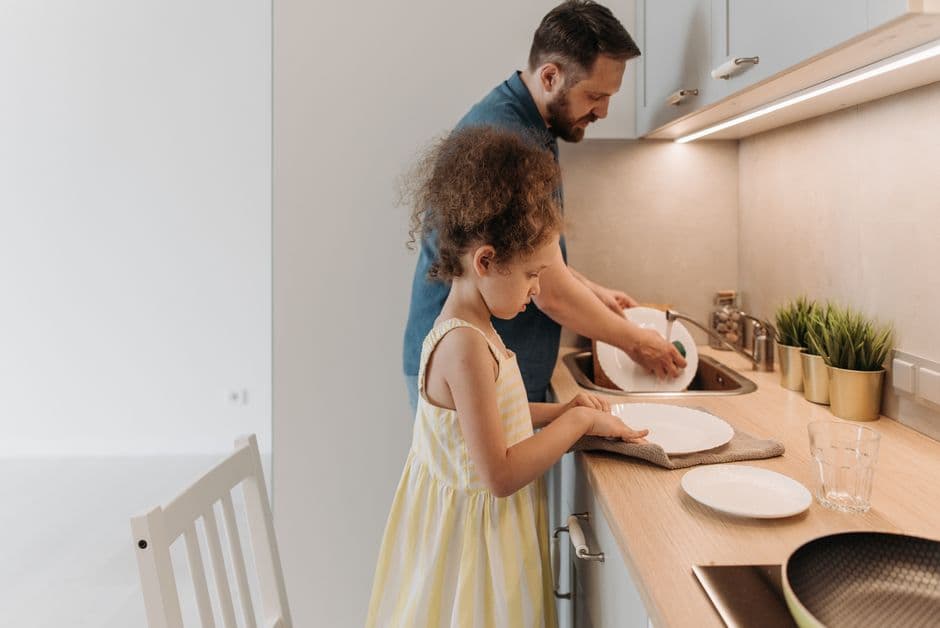 Father and daughter bonding while washing dishes together in a modern kitchen.